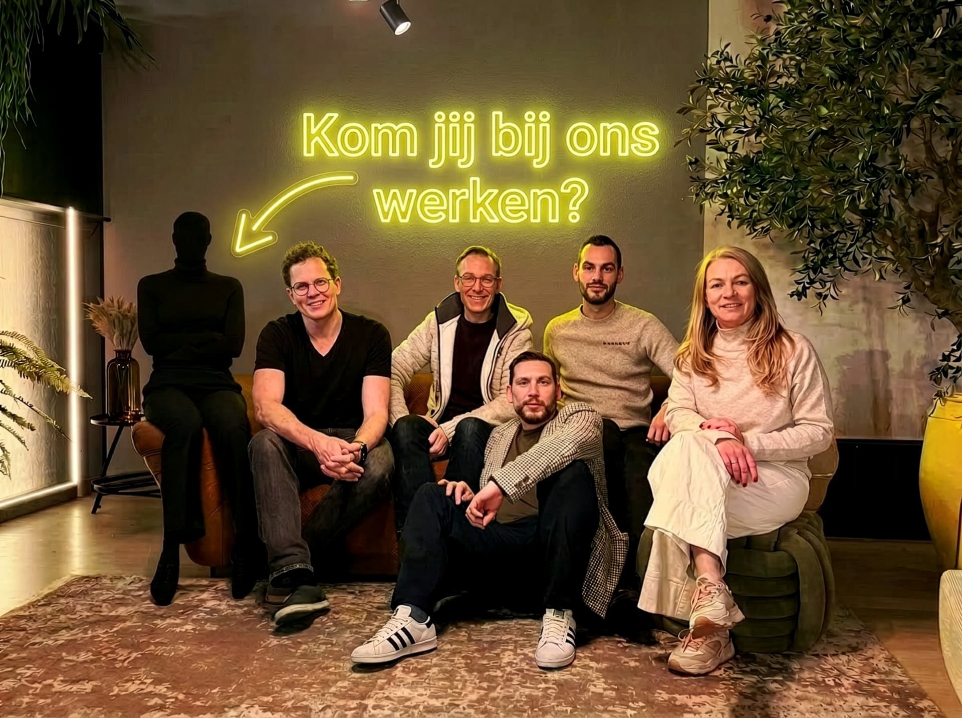 Het team van WBSO.ai op een bank, met een schim van een medewerker ernaast. Daarnaast staat een neon-tekst: Kom jij bij ons werken?